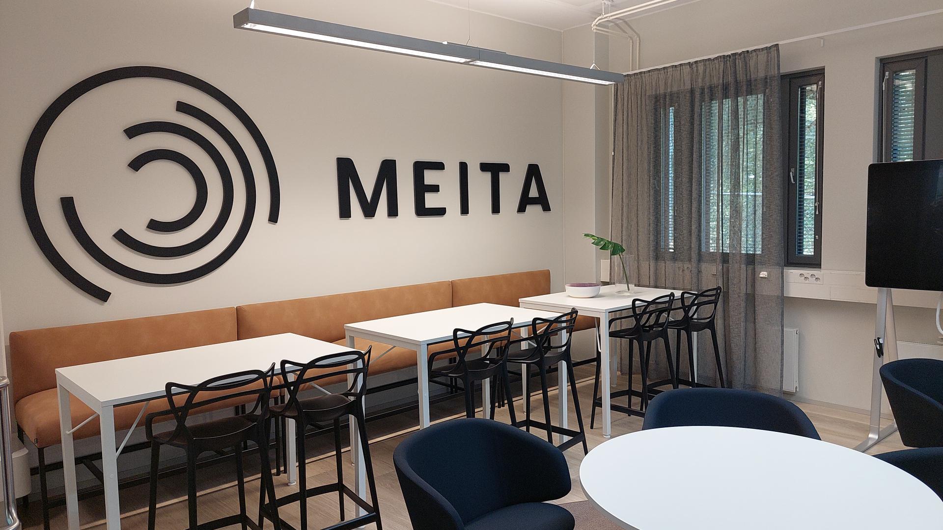 Tässä kuvassa on Meitan logo ja teksti Lappeenrannan toimiston kahvion seinällä sekä pöytiä ja tuoleja