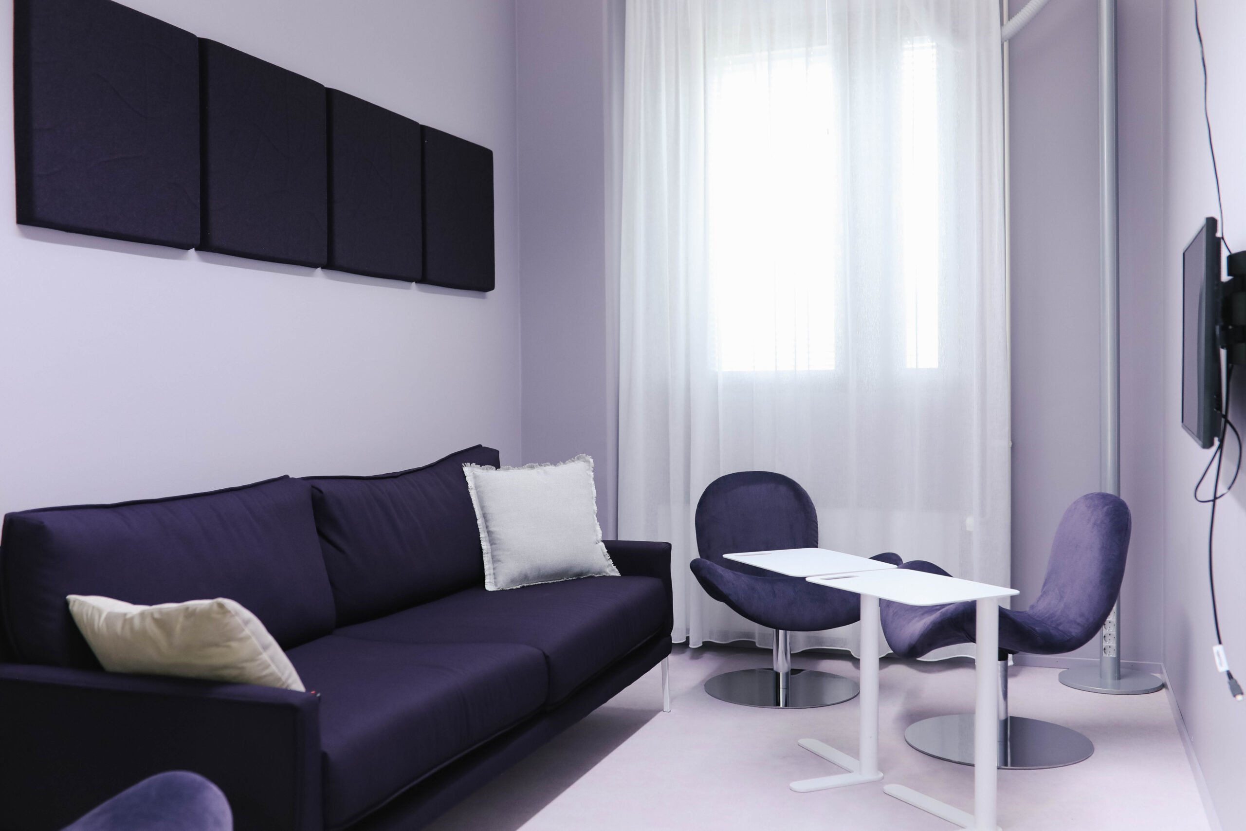 Tässä kuvassa on Meitan Lappeenrannan toimiston työskentelytila, jossa on sohva, tuoleja, pöytä, näyttö sekä äänieristelevyt seinällä